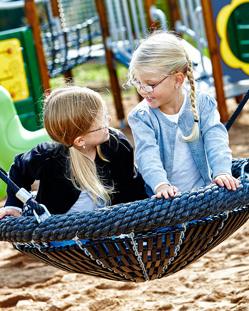 Two children are sitting on a large basket swing and swinging.